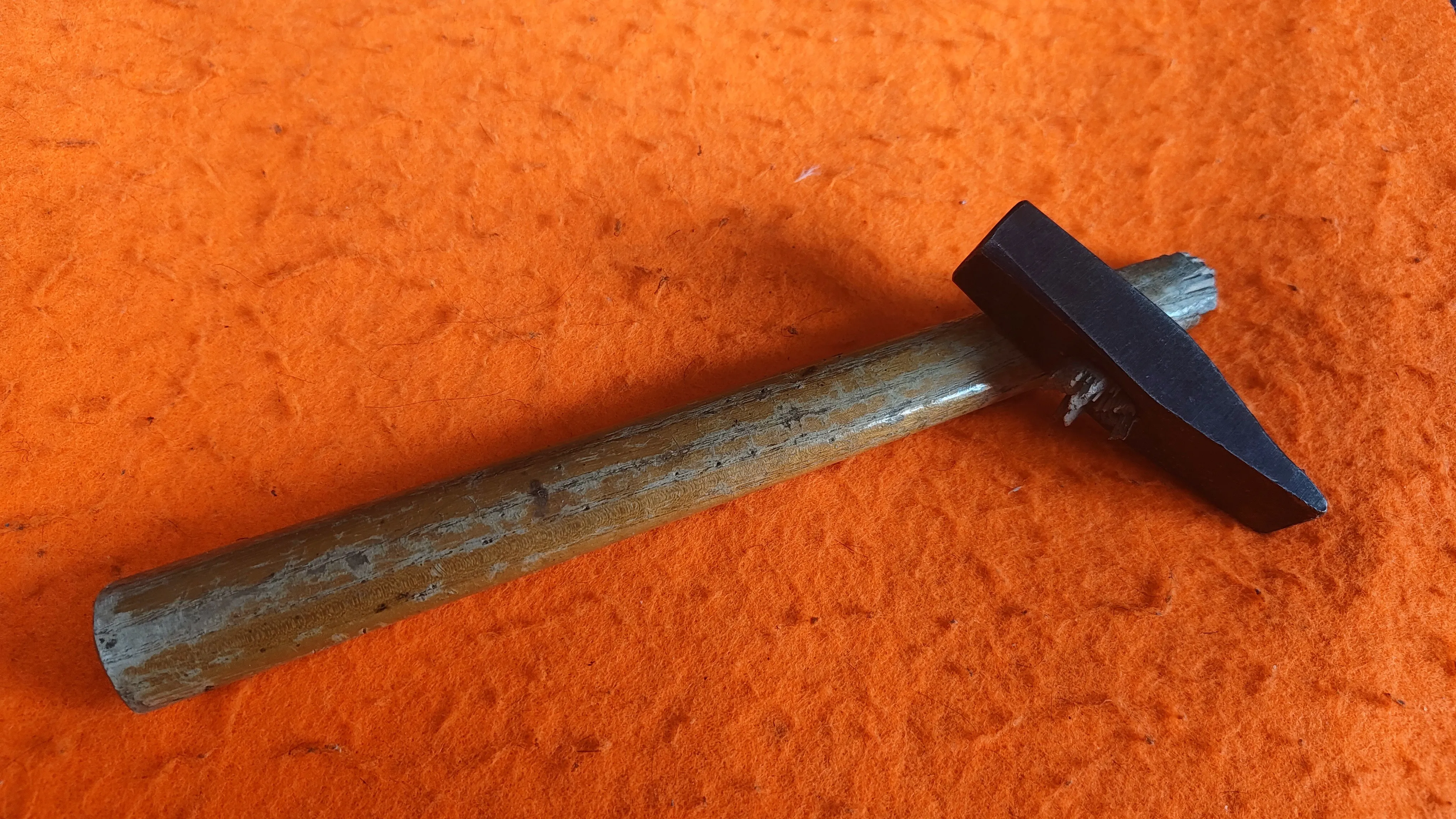 Ein Foto eines Hammers, dessen Kopf am Stil abgebrochen ist vor orangem Filzhintergrund